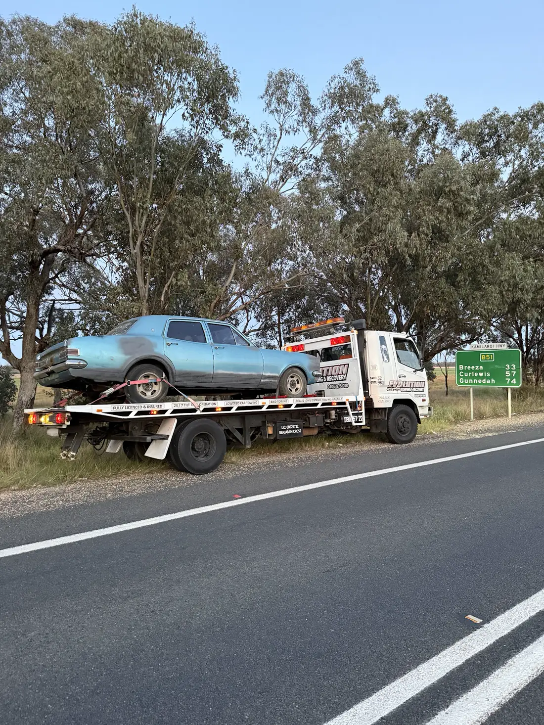 Classic HK Holden on the Evolution tilt tray beside a highway distance sign