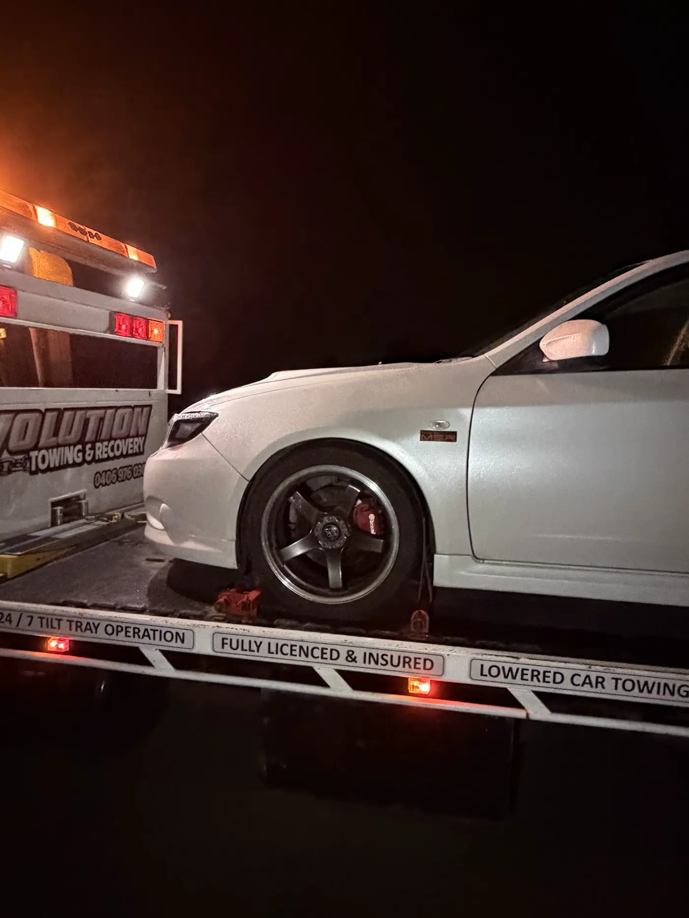 White Subaru WRX secured on the Evolution tilt tray at night