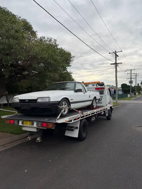White Ford XF ute loaded on the Evolution tilt tray in a leafy street