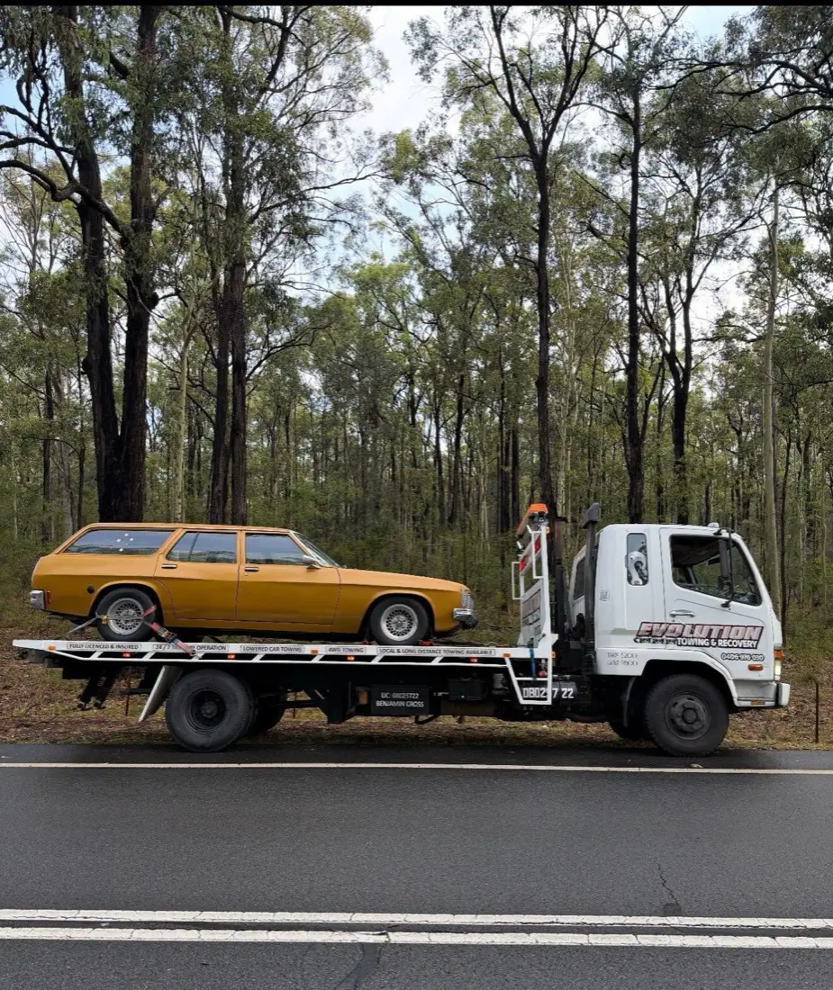 Gold HQ Holden wagon loaded on the Evolution tilt tray beside a bush highway
