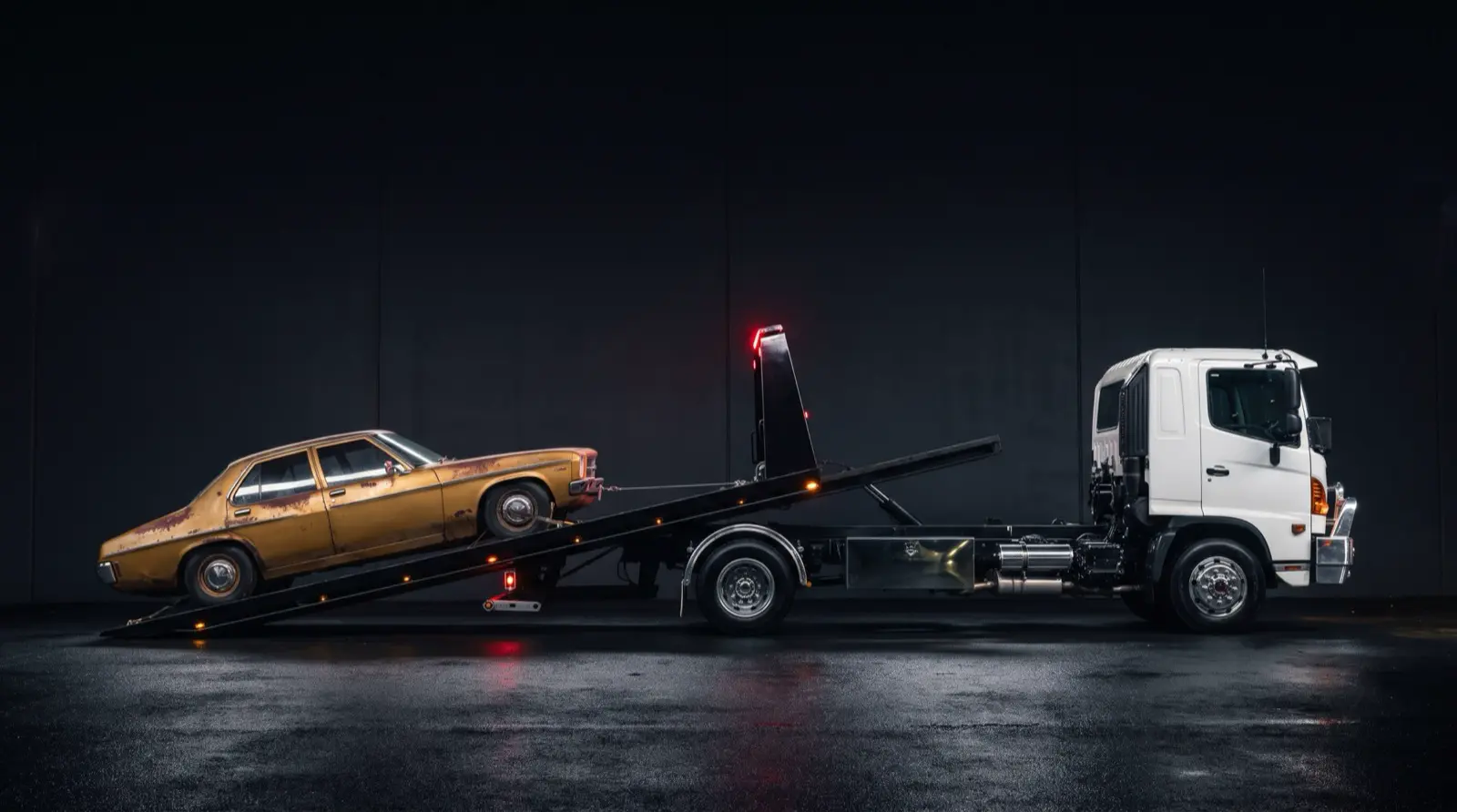 Side profile of the tilt tray lowered to the ground while a classic sedan is winched onto the deck
